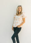 Model wearing jeans with a white and coral embroidered floral top with bubble short sleeves. 