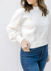 Model wearing jeans with an ivory top with textured accents, long sleeves and a slightly cropped fit