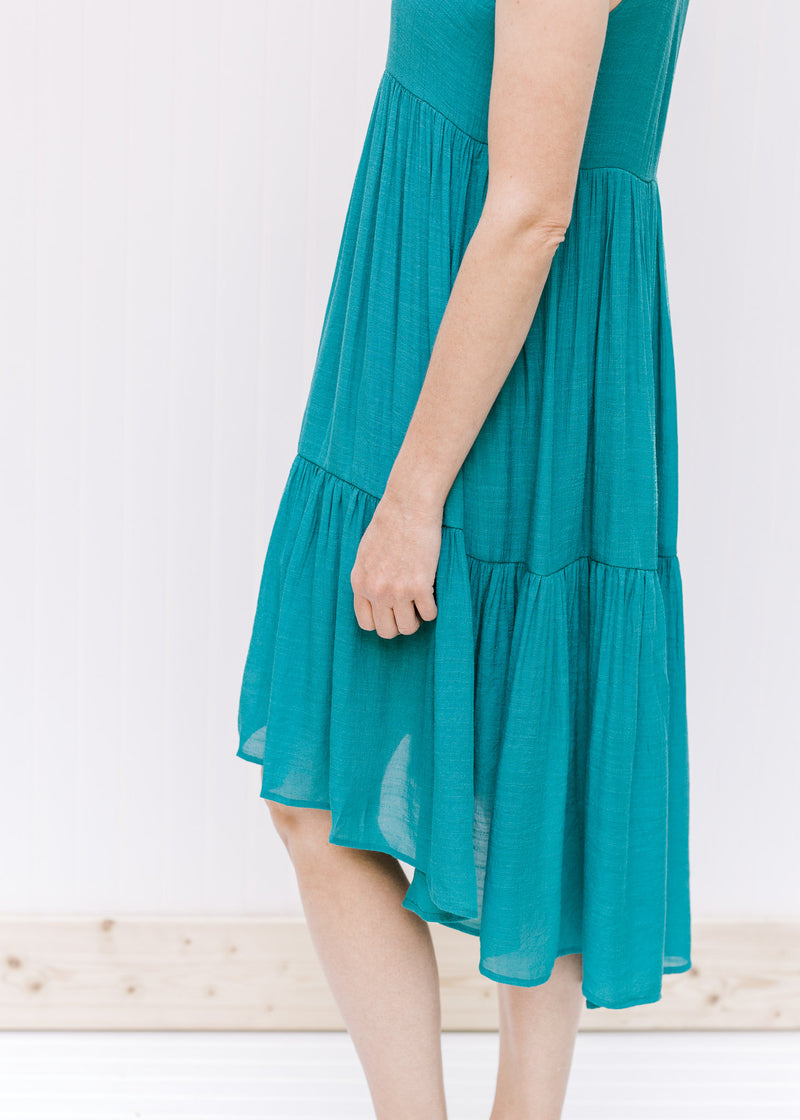 Close up of hi-low silhouette on a tiered deep teal sleeveless dress. 
