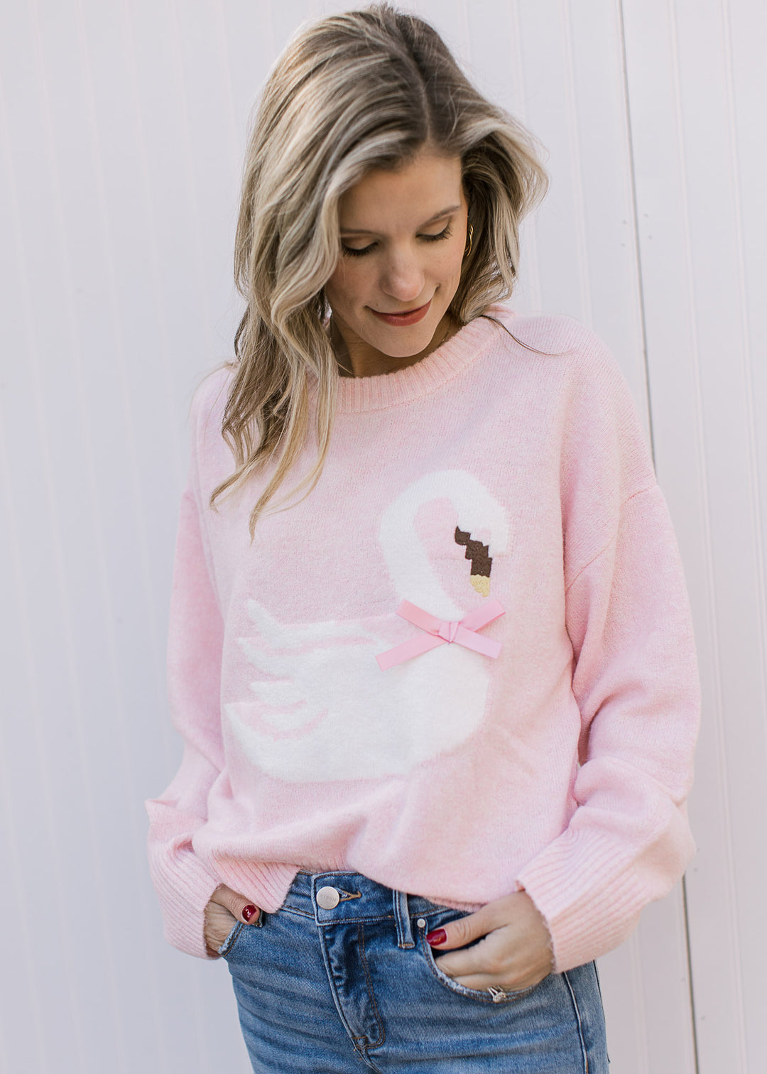 Model wearing a pale pink sweater with a white swan, stitched beak and pink bow detail.