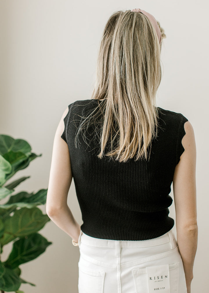 Back view of Model wearing a black ribbed top with scalloped neck and at sleeveless straps. 