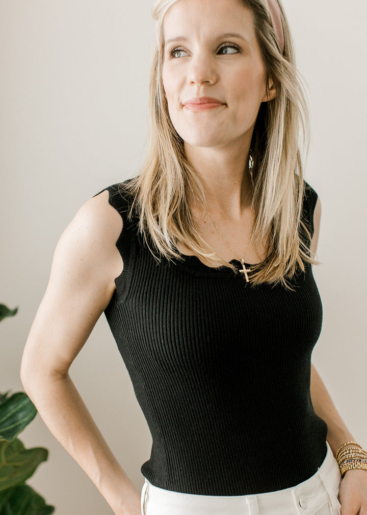 Model wearing a fitted black ribbed top with scalloped square neck and at sleeveless straps. 