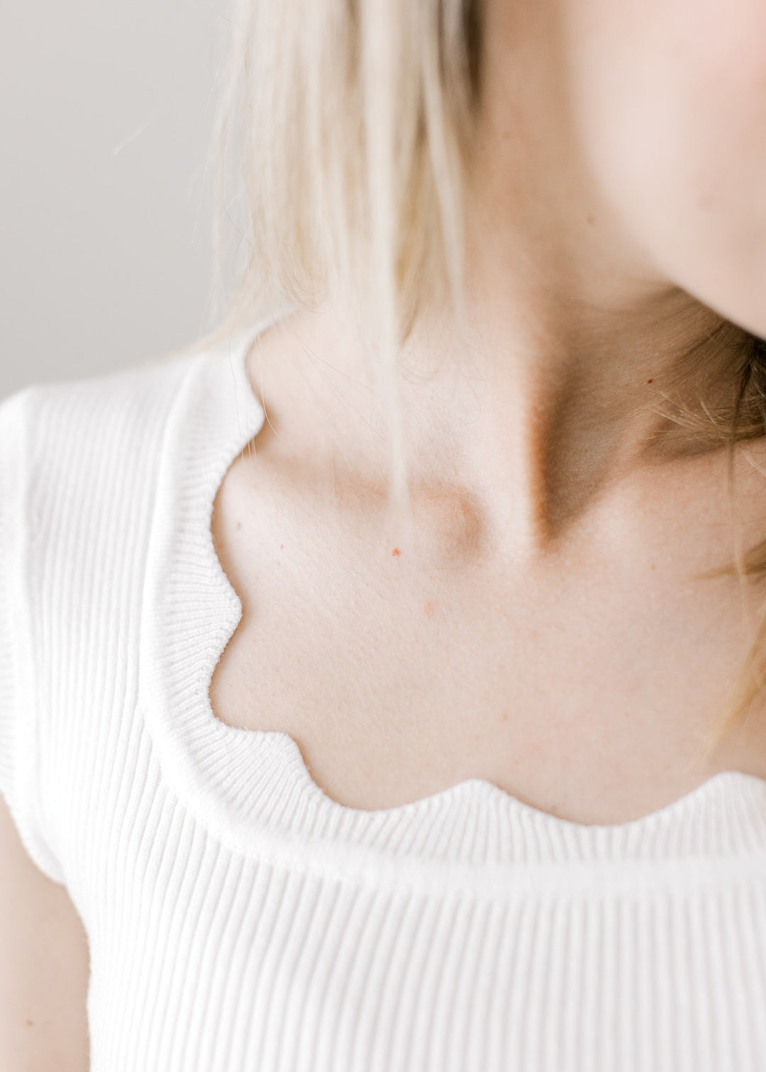 Close up of scalloped square neckline and ribbed material on a fitted white sleeveless top. 