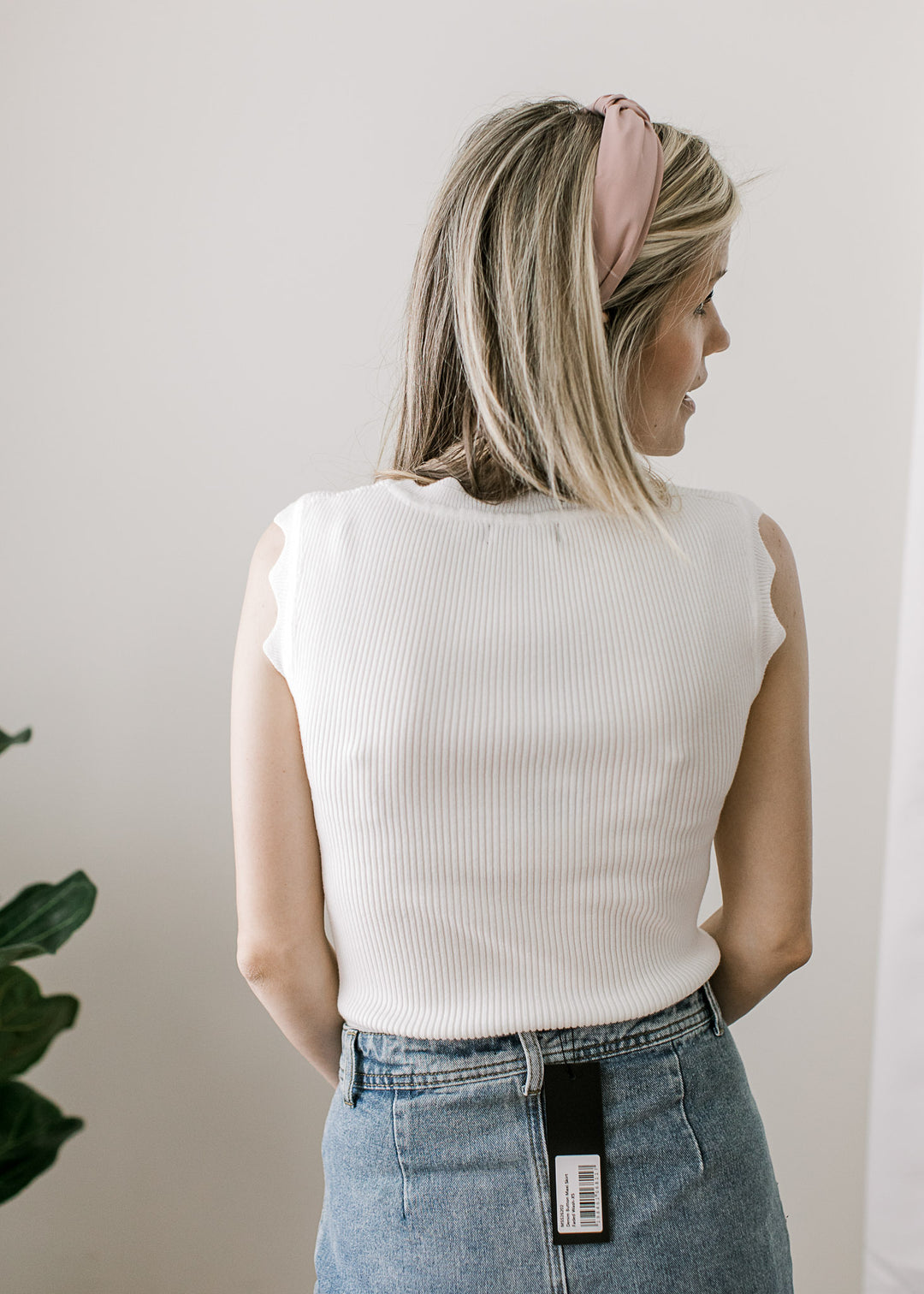 Back view of model wearing a white ribbed top with scalloped neck and sleeveless straps. 