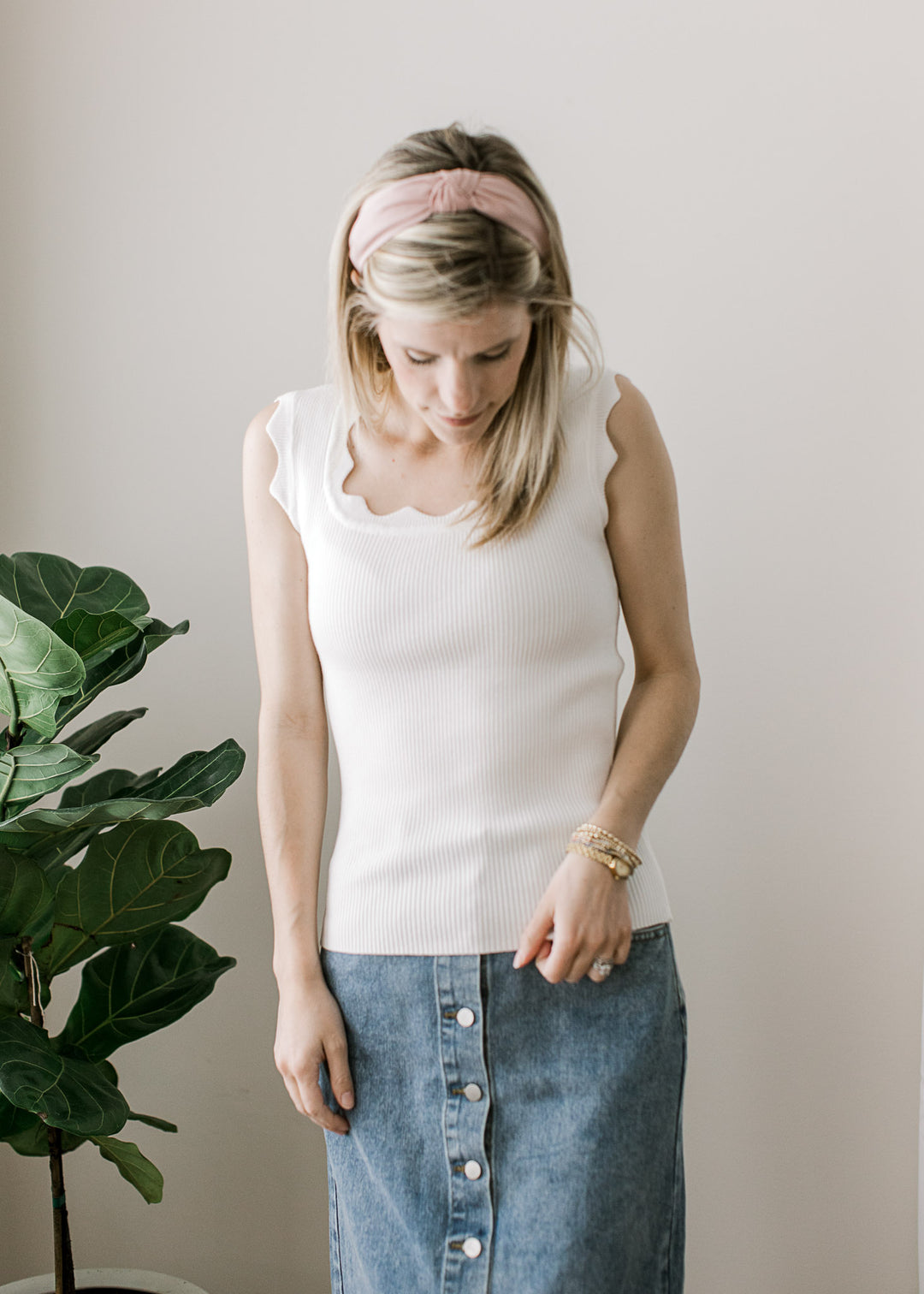 Model wearing a fitted white ribbed top with scalloped square neck and at sleeveless straps. 