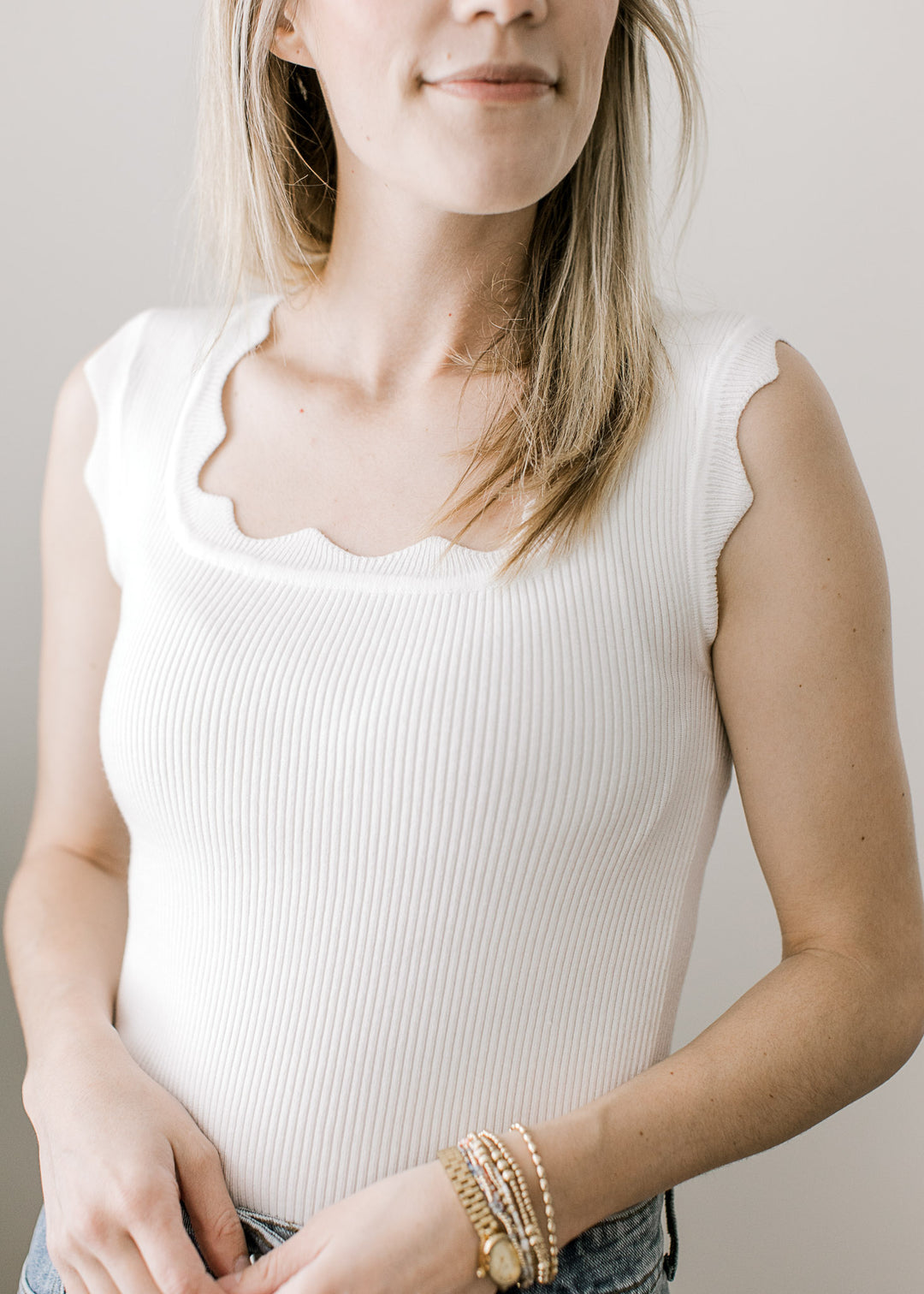 Model wearing a white ribbed top with scalloped square neck and at sleeveless straps. 