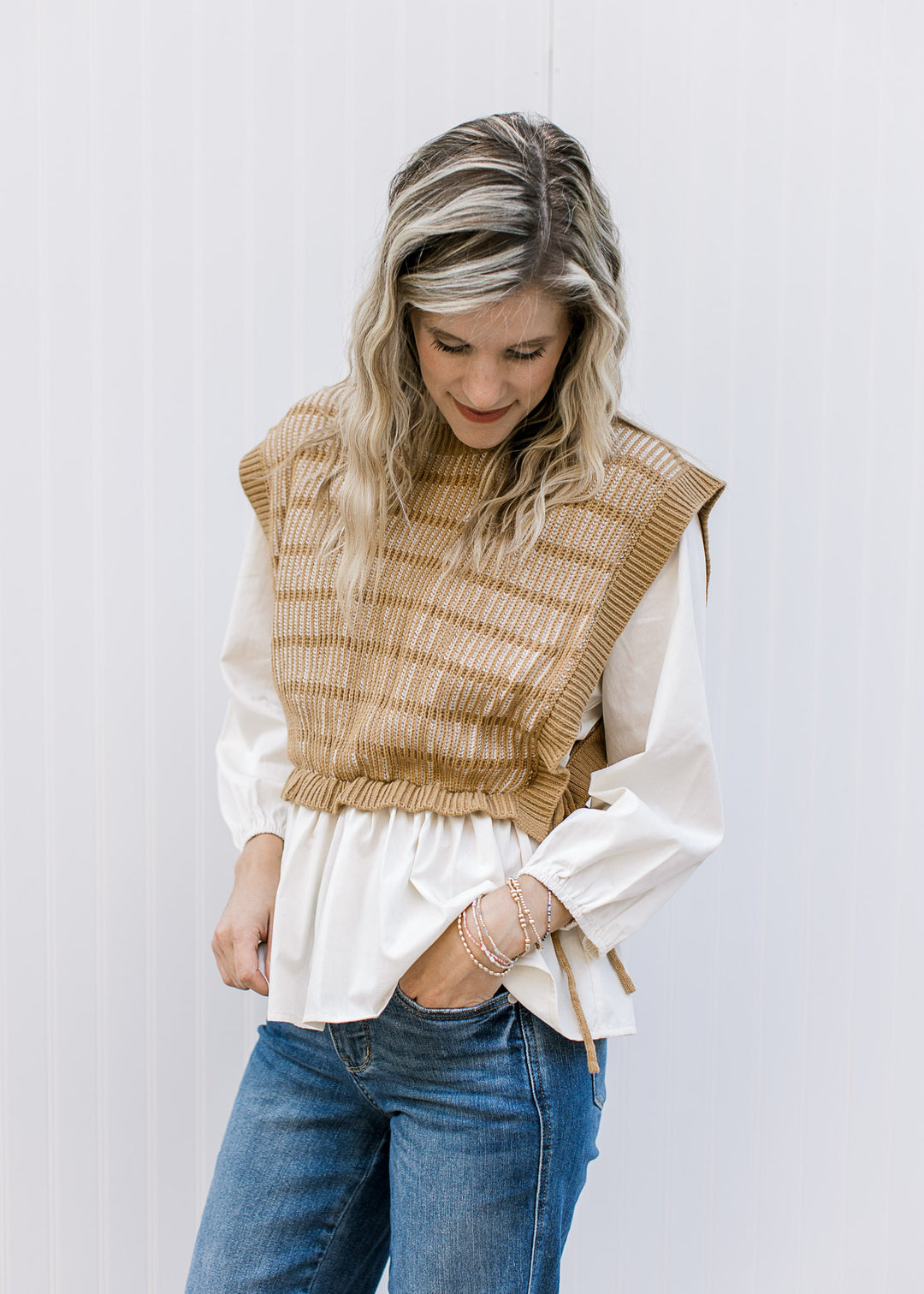 Model wearing a cream blouse with an attached caramel and cream vest with ties at the side. 