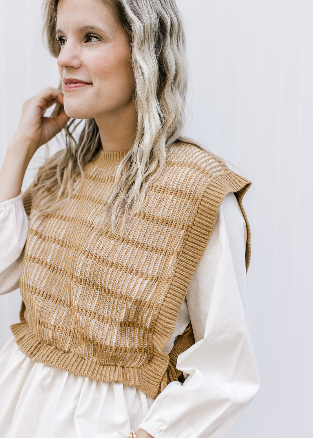 Model wearing a long sleeve cream blouse with an attached caramel and cream vest and round neck.