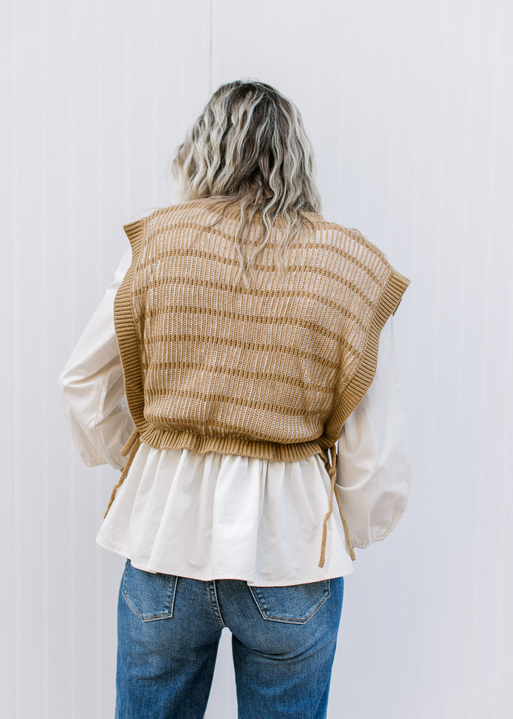 Back view of Model wearing a long sleeve cream blouse with a caramel and cream attached vest. 