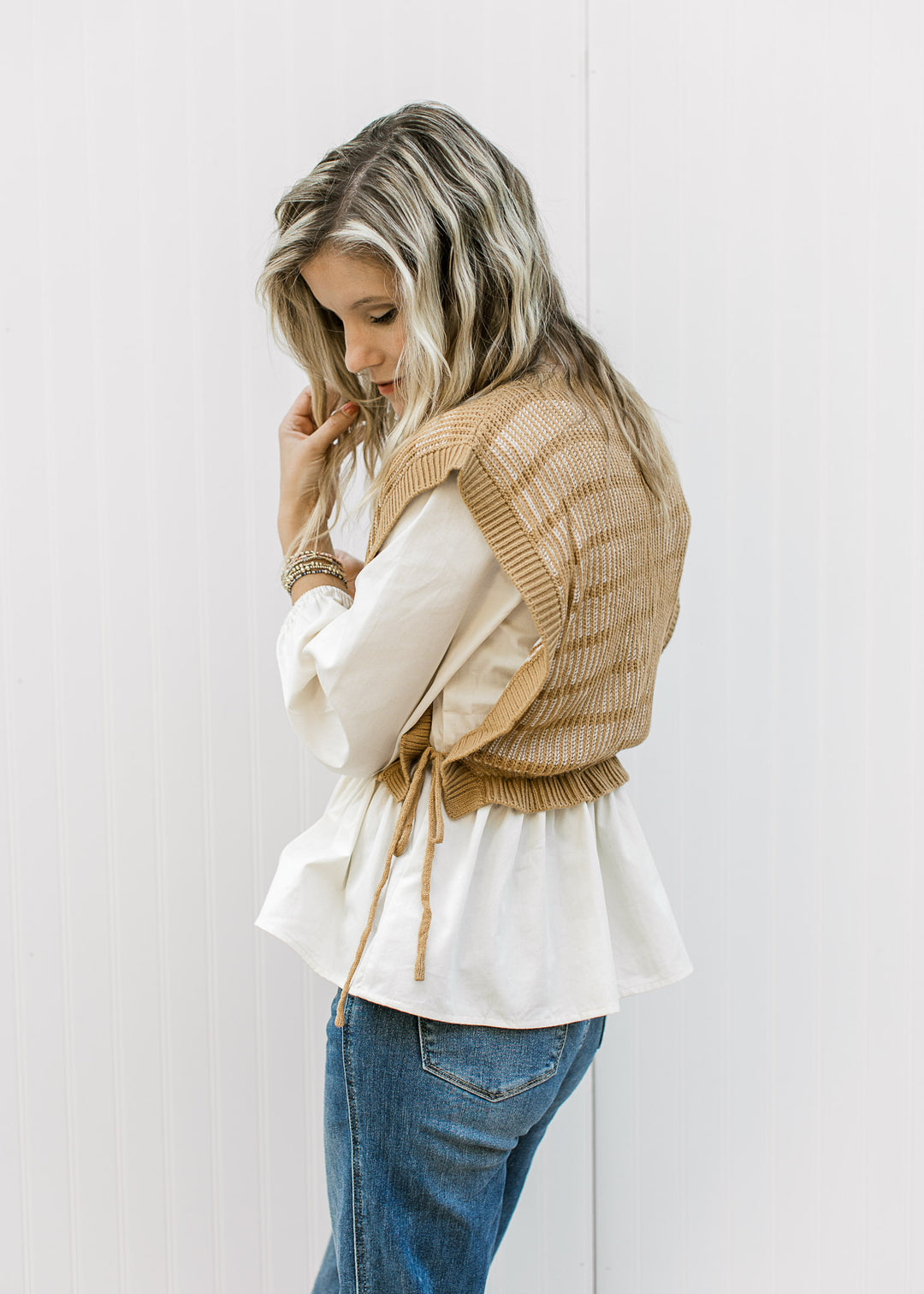 Side view of Model wearing a long sleeve cream blouse with a caramel and cream attached vest. 