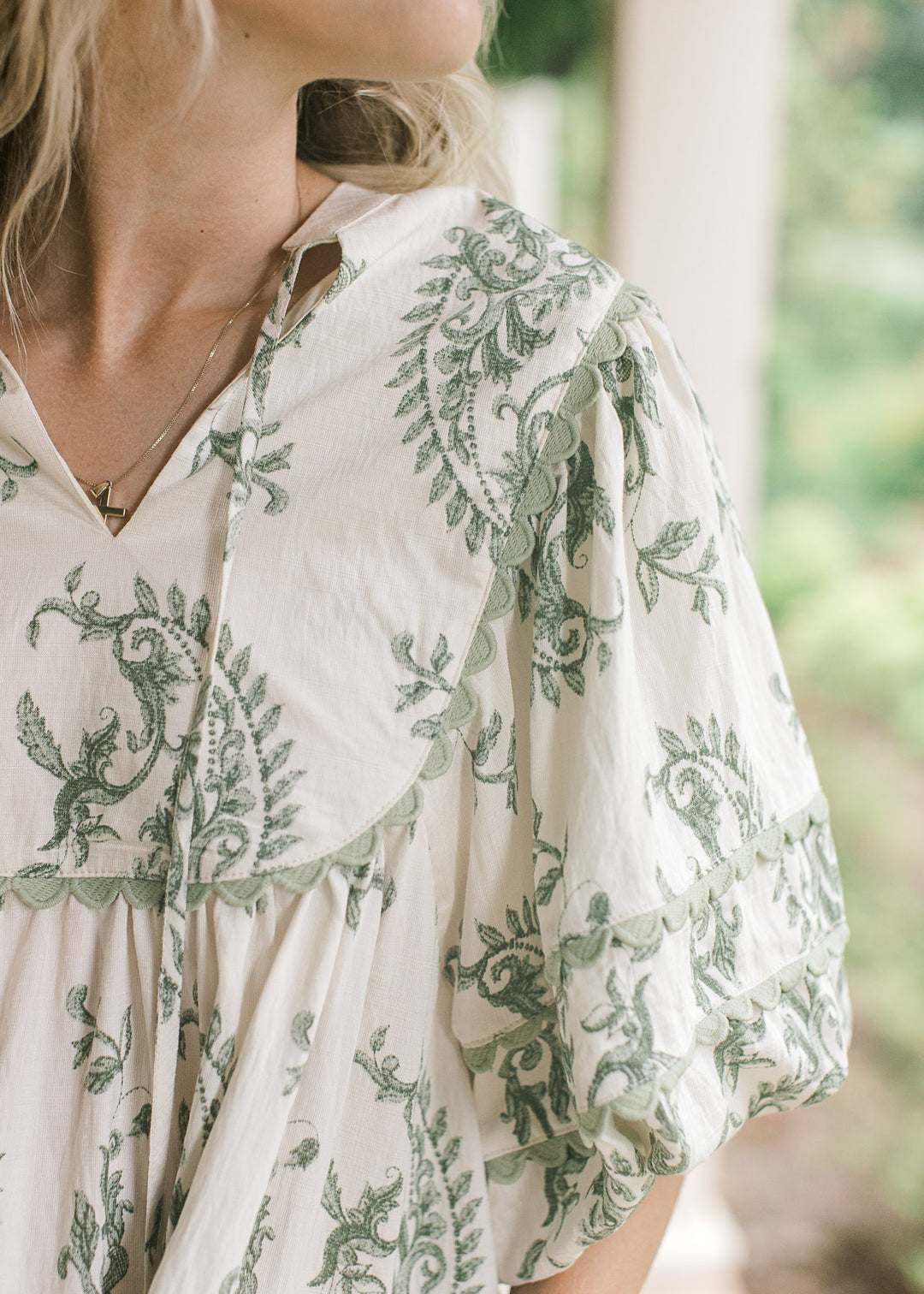 Close up of sage scalloped detail and v-neck with a tie on a cream top with olive floral pattern.