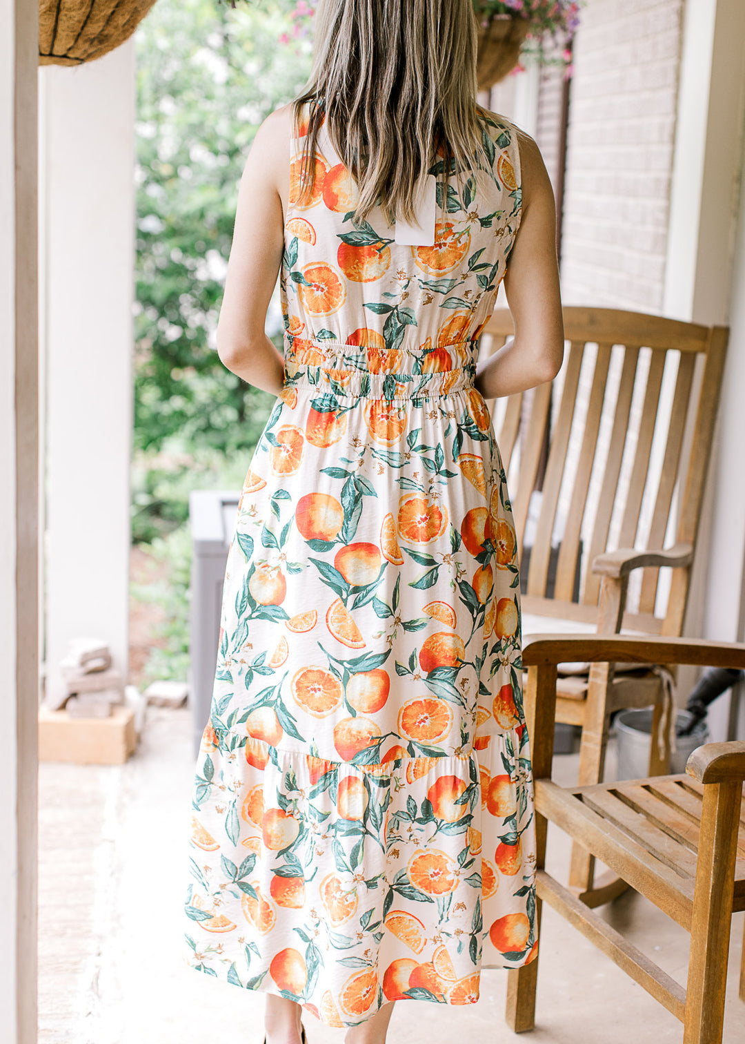 Back view of Model wearing a cream midi with oranges and green leaf print and smocked waist. 
