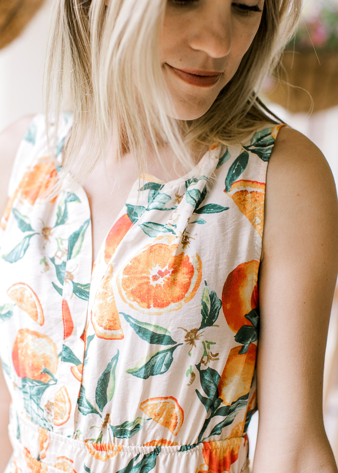 Close up of v-neckline on a sleeveless cream midi ith oranges and green leaf pattern. 