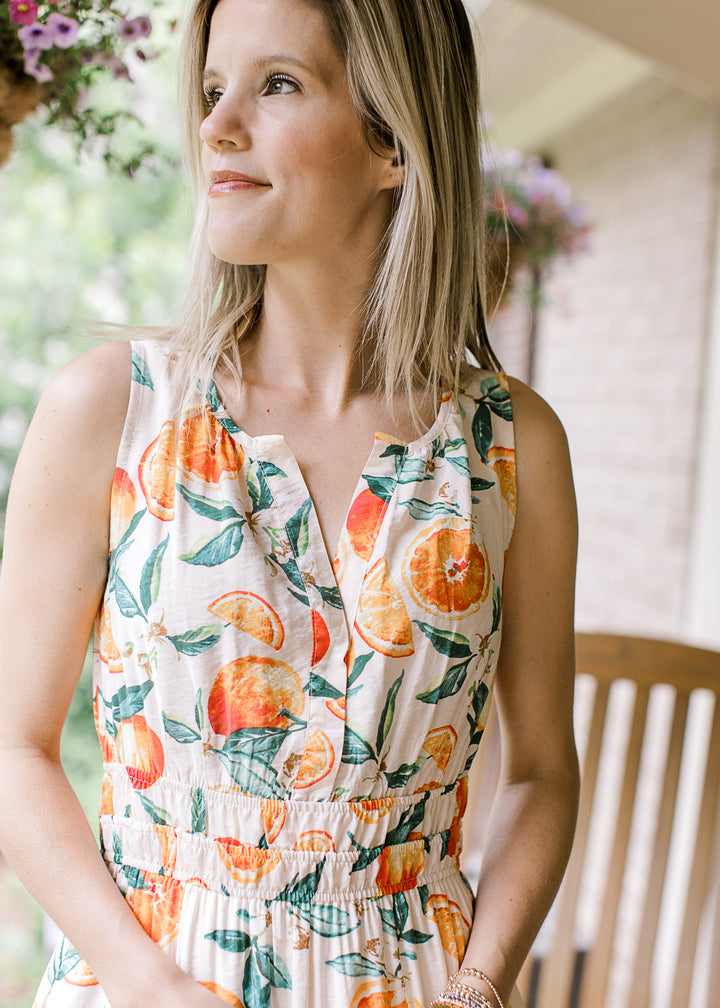 Model wearing a cream sleeveless midi with a smocked bodice and green leaf design with oranges.  