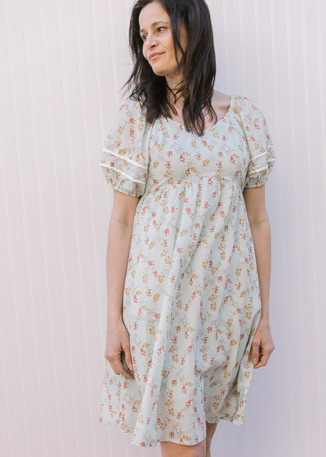 Model wearing a lightweight sage dress with rose and mustard floral, v-neck, bubble short sleeves. 