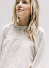 Close up view of cream top with a neutral ditzy floral pattern, smocked detail and long sleeves. 