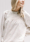 Model wearing a cream top with a neutral ditsy floral, smocked detail and long sleeves. 