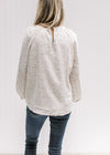 Back view of Model wearing a cream top with a neutral ditsy floral, smocked detail and long sleeves.