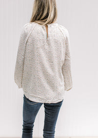 Back view of Model wearing a cream top with a neutral ditsy floral, smocked detail and long sleeves.
