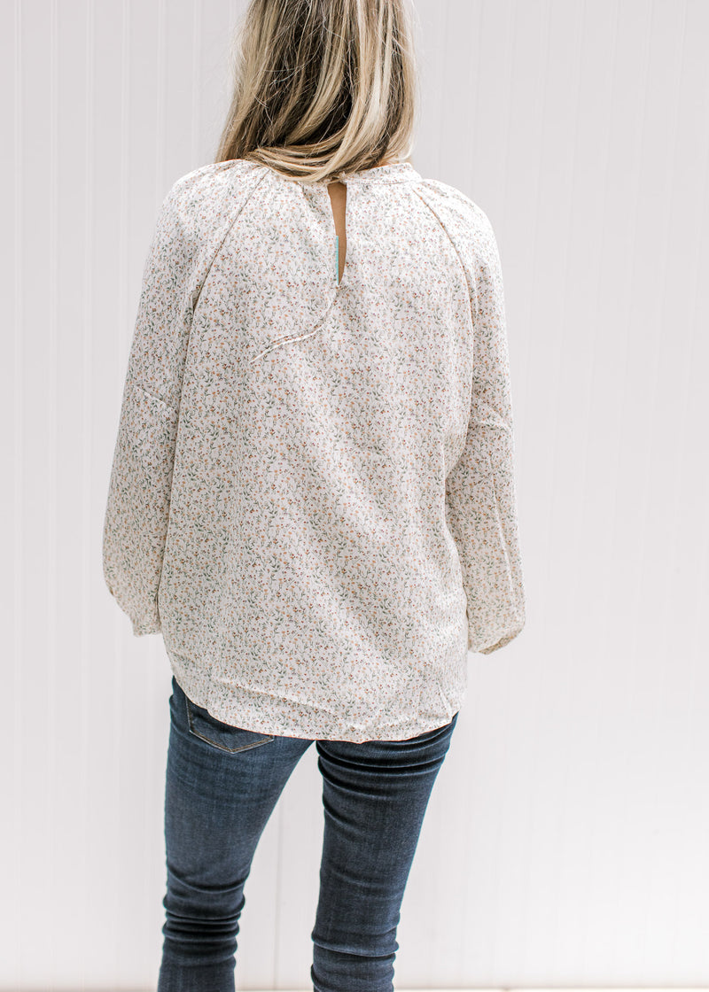 Back view of Model wearing a cream top with a neutral ditsy floral, smocked detail and long sleeves.