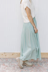 Side view of Model wearing a sage polyester midi with a flowy fit and an elastic waist. 