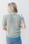 Back view of Model wearing a knit sage sweater with a round neck and eyelet detailed short sleeves. 