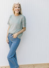 Model wearing jeans with a knit sage sweater with a round neck and eyelet detailed short sleeves. 