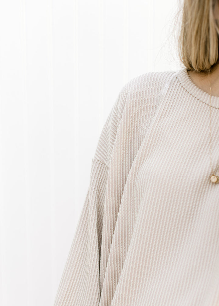 Close up of corded material on a tan loose fit top with long sleeves and split sides. 