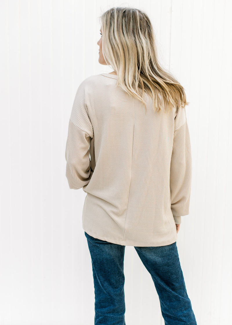 Back view of model wearing a tan top with a corded material, long sleeves and split sides. 
