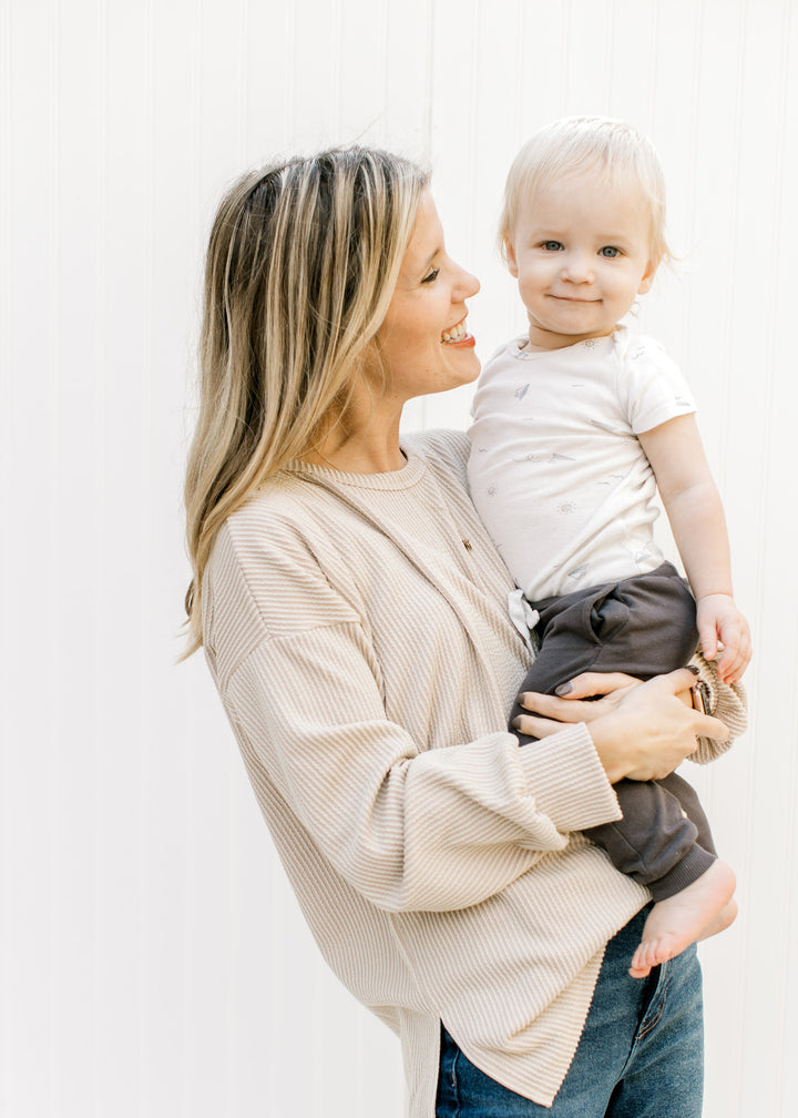 Model holding a baby wearing a tan corded top with long sleeves and split sides.