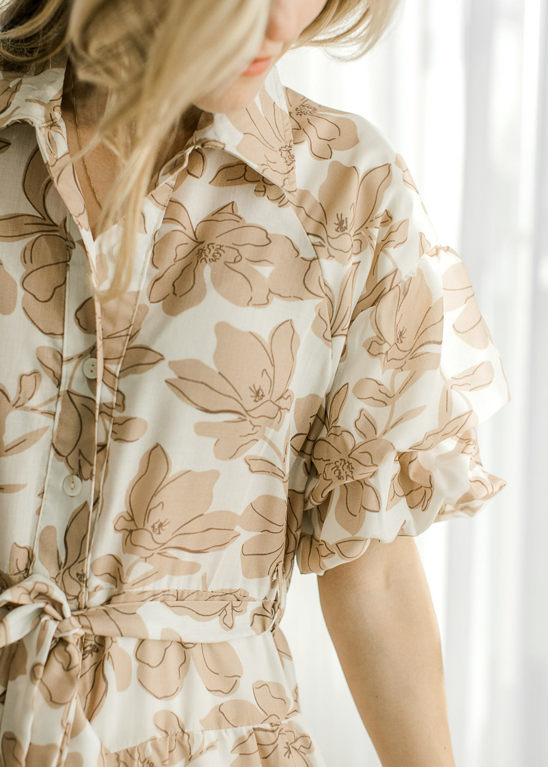 Close up of bubble short sleeves, tie waist and button front on a white midi with tan floral. 