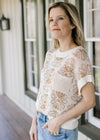 Model wearing a cream knit sweater with tan flowers, patch pockets and capped sleeves.