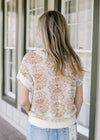 Back view of Model wearing a cream knit sweater with tan flowers, patch pockets and capped sleeves.