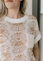 Close up of tan flowers and patch pocket on a cream sweater with ribbed neck, cuff and hem.