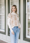 Model wearing a cream mockneck top under a cream cap sleeve sweater with tan flowers.