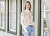 Model wearing jeans and a cream mock neck top under a cream sweater with tan flowers.