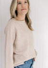 Model wearing a tan textured sweater with long sleeves and a crew neckline. 