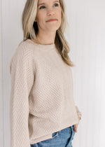 Model wearing a tan textured sweater with long sleeves and a crew neckline. 