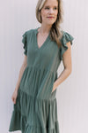 Close up of v-neck and ruffle cap sleeves on a hunter green midi with pockets. 