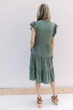 Back view of Model wearing a hunter green tiered midi with ruffle cap sleeves and pockets.