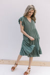 Model wearing heels with a hunter green tiered midi with ruffle cap sleeves and a v-neck.