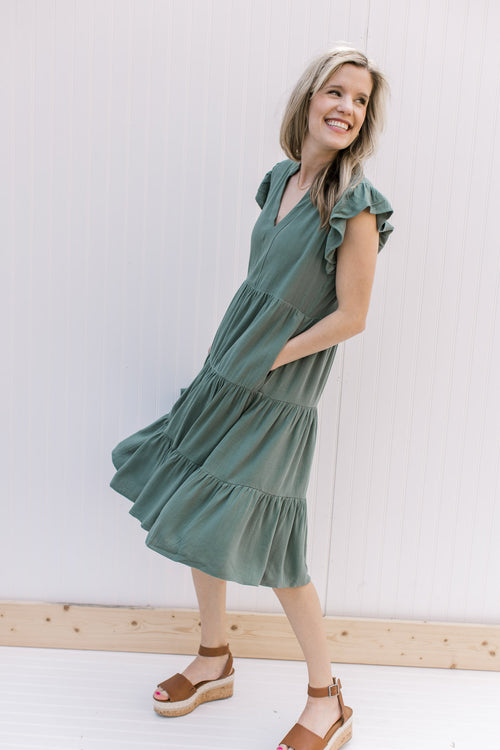 Model wearing a hunter green tiered midi with ruffle cap sleeves and pockets.