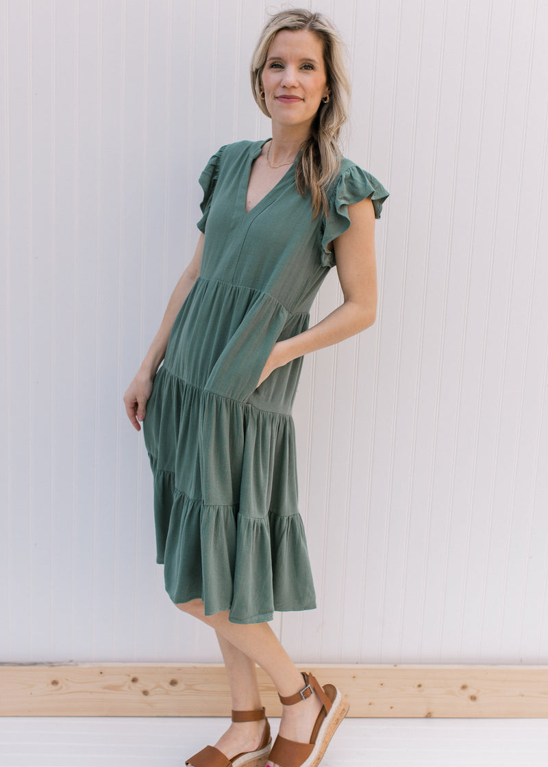 Model wearing a hunter green tiered midi with ruffle cap sleeves and a v-neck.