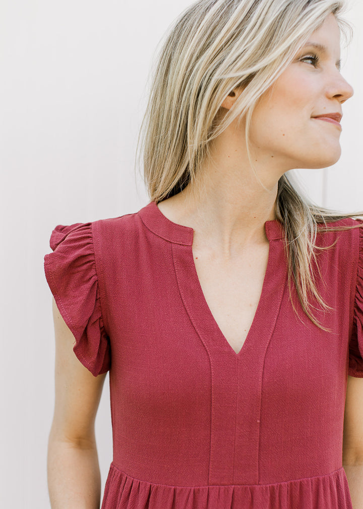 Close up of clutter cap sleeves and v-neckline on a maroon knee length dress with tiers. 