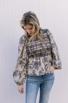 Model wearing a taupe with black floral top with a smocked bodice and long puff sleeve.