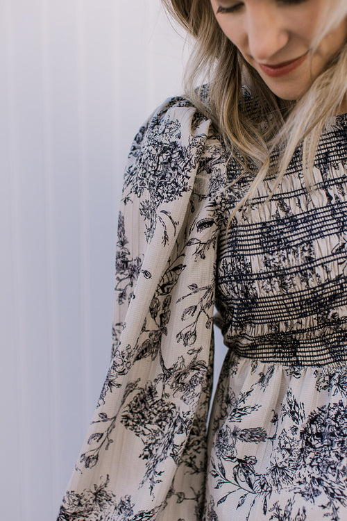 Close up of smocked bust and pleated shoulder on long sleeves of a taupe top with black floral.