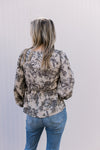 Back view of Model wearing a taupe top with black floral, a smocked bodice and long puff sleeve.