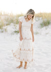 Model is wearing a cream dress with taupe embroidered floral, smocked bodice and ruffle cap sleeve. 