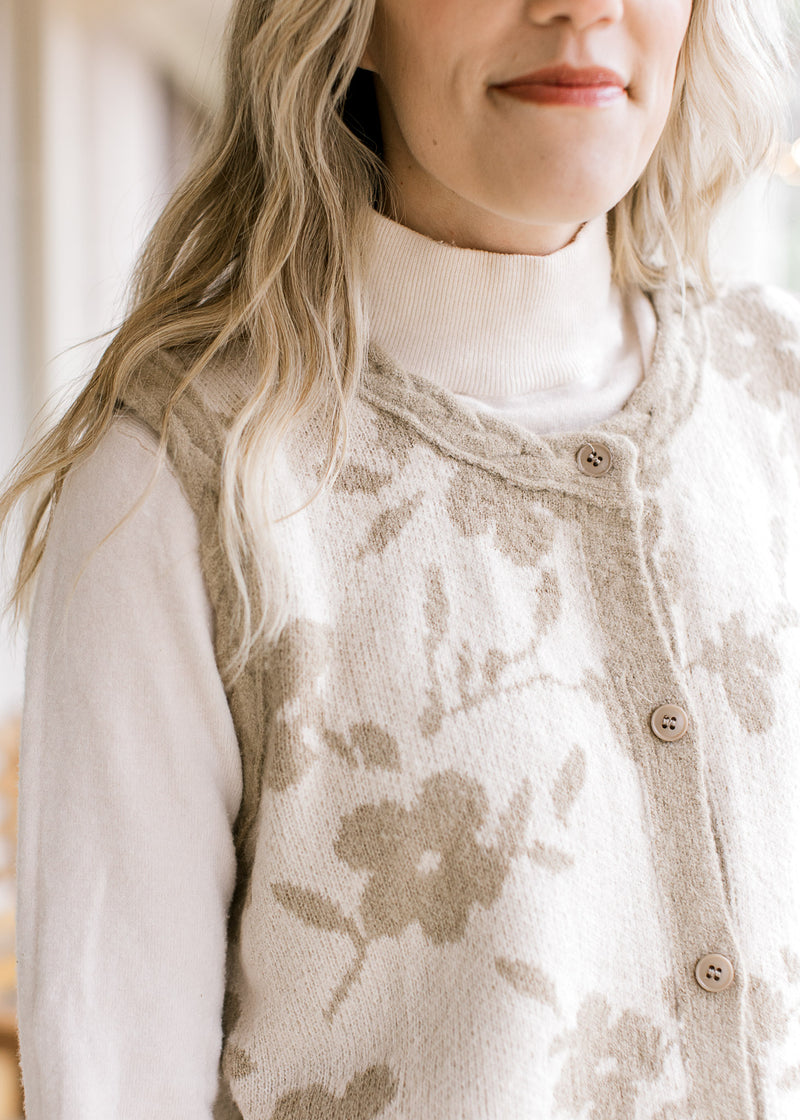 Close up of buttons and braided taupe edging on a cream sleeveless cardigan with flowers.