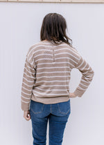 Back view of Model wearing a taupe sweater with cream zig zag stripes and a zipper in the back. 